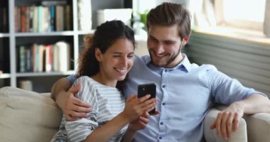 Mutlu milenyum çifti evdeki koltukta otururken akıllı telefon kullanıyor.