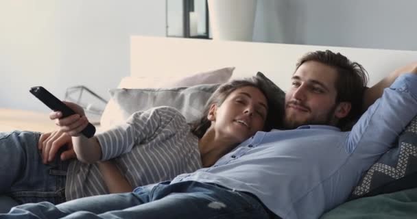 Relaxed couple lying in bed holding remote control watching tv — Stock Video