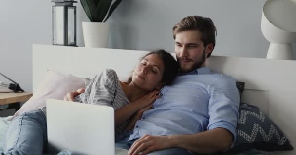 Pareja casual joven relajándose tumbado en la cama mirando portátil — Vídeo de stock