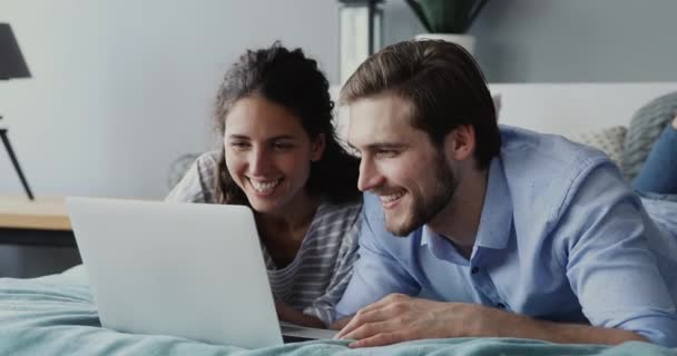 Happy couple using laptop watching online show lying in bed — Stock Video
