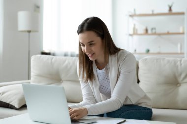 Evdeki dizüstü bilgisayarda internette gezinen mutlu genç kadın.