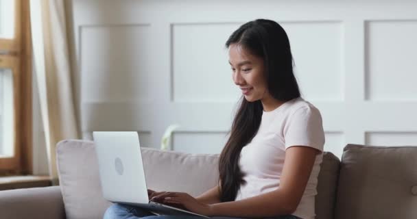 Χαμογελώντας εστιασμένη ασιατική εθνικότητα νεαρή γυναίκα χρησιμοποιώντας υπολογιστή στο σπίτι. — Αρχείο Βίντεο