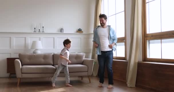 Молодий батько танцює на підігрітій дерев'яній підлозі з маленьким сином . — стокове відео