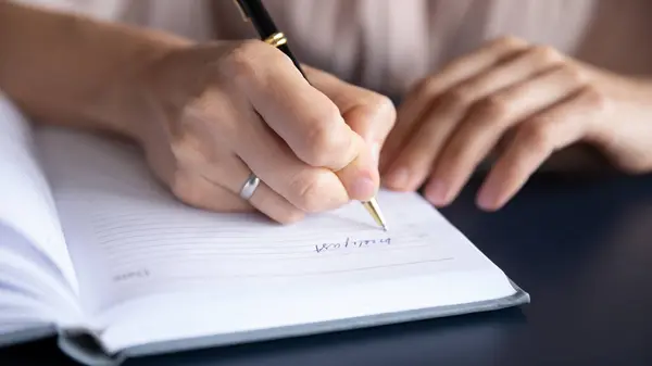 Close up female hand holding pen, writing in notebook — Stock Photo, Image