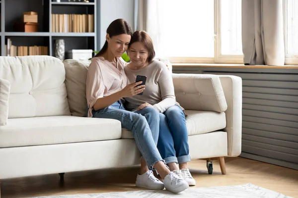 Gelukkig ouder moeder en volwassen dochter met behulp van telefoon samen — Stockfoto