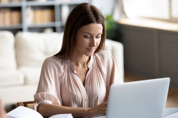 Fokuserad kvinna som arbetar på bärbar dator online, sitter vid skrivbordet — Stockfoto