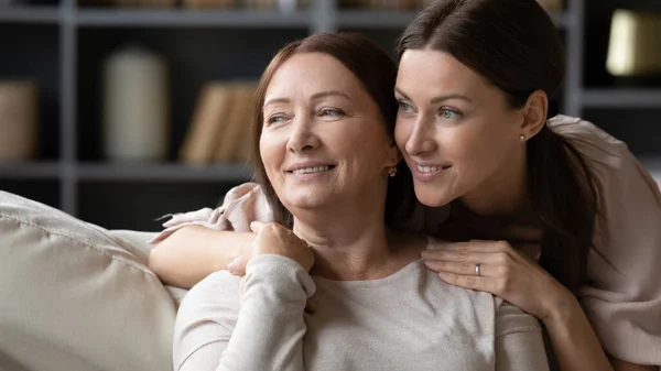 Sonriente madre madura e hija adulta abrazándose, mirando en la distancia — Foto de Stock