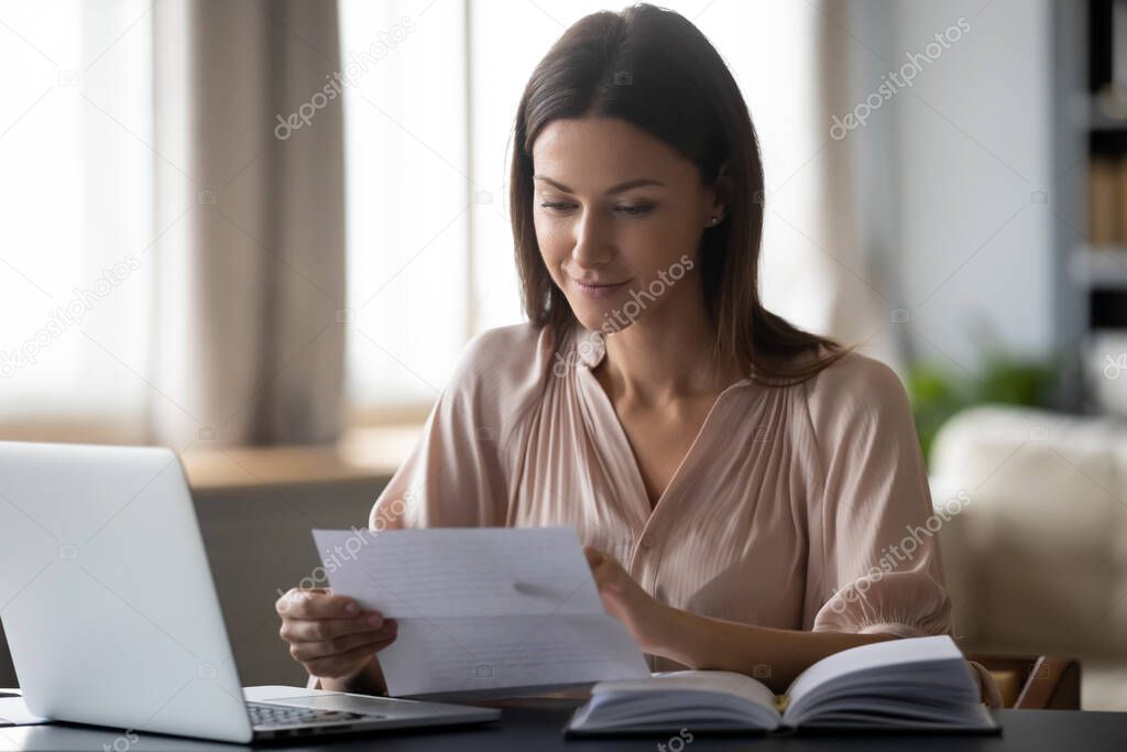Young woman holding paper, reading good news in letter at home