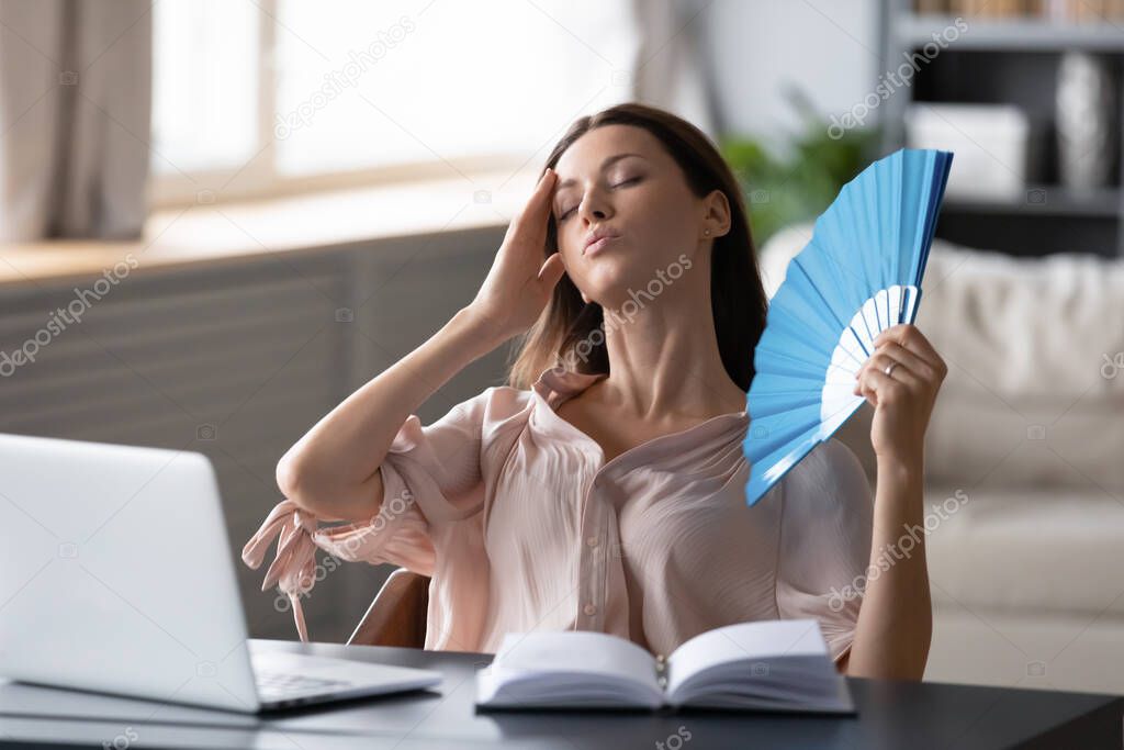 Overheated woman waving fan, touching forehead, suffering from heating