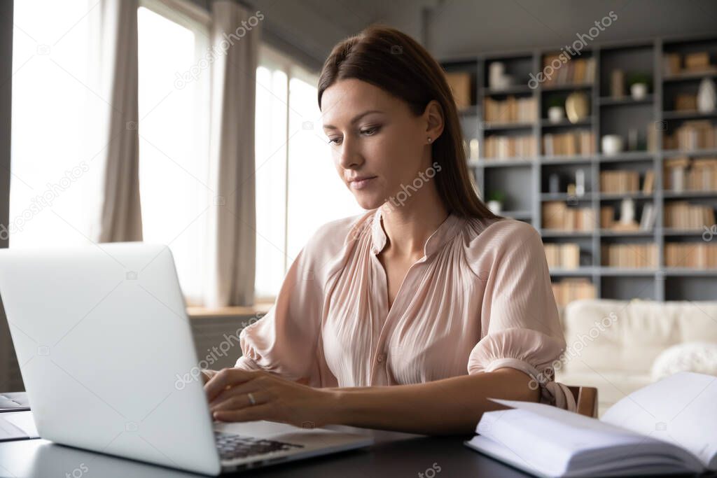 Focused woman working on laptop, sitting at desk at home