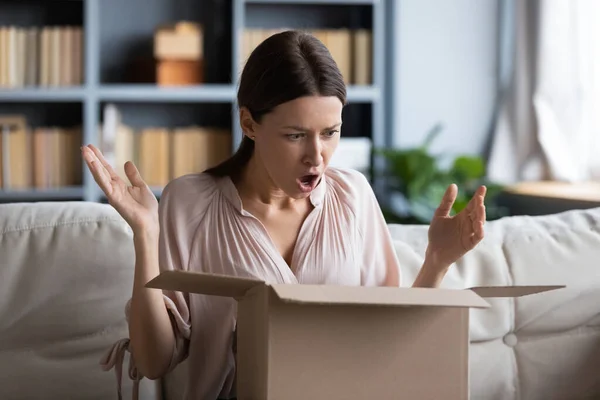 Θυμωμένη σοκαρισμένη νεαρή γυναίκα ξεπακετάρει δέμα στο σπίτι — Φωτογραφία Αρχείου