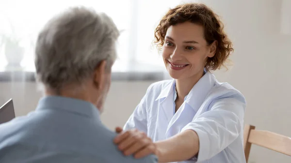 Glimlachende vrouwelijke arts geruststellende ondersteunende senior patiënt in het ziekenhuis — Stockfoto