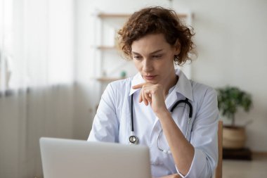 Bilgisayarda çalışan konsantre genç kadın doktor online araştırma yapıyor.