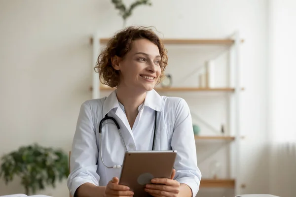 Smiling young female professional doctor holding digital tablet looking away — Stock Photo, Image