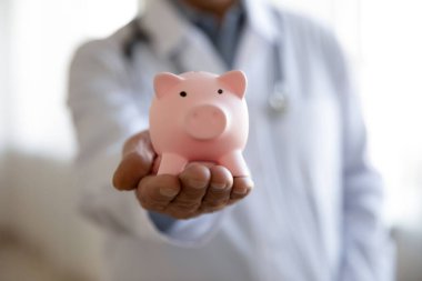 Yaşlı erkek doktor kumbarayı tutuyor, manzarayı kapat.