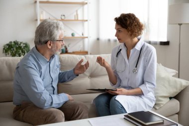 Kadın doktor, evde sağlık kontrolü sırasında kıdemli hastaya danışmanlık yapıyor.