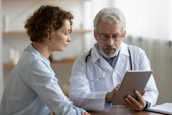 Yaşlı doktor dijital tablet kullanan genç bir kadına danışıyor. — Stok fotoğraf