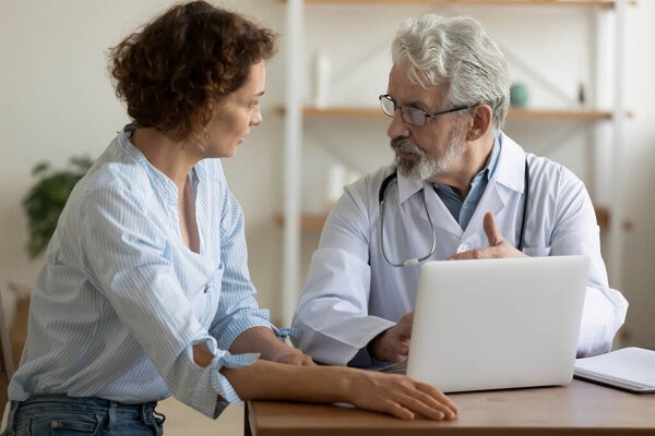 Senior male professional physician consulting female patient using laptop