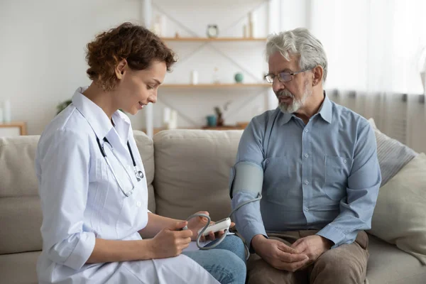 Vrouwelijke arts onderzoekt oude patiënt die thuis de bloeddruk controleert — Stockfoto