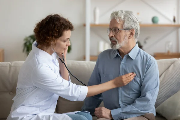 Женщина-врач, держащая стетоскоп, слушает старую пациентку во время посещения дома — стоковое фото