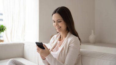 Kafkasyalı kız koltuğa oturup cep telefonu aleti kullanıyor.