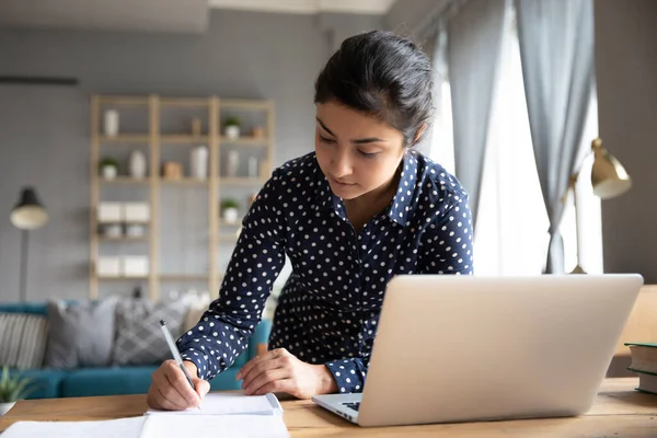 Giovane studente indiano concentrato che scrive appunti dal seminario online . — Foto Stock