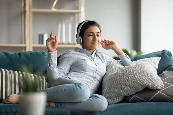 Gelukkig indiaans meisje rusten op gezellige bank, luisteren naar muziek. — Stockfoto