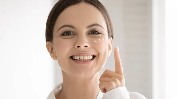 Retrato de mujer joven sonriente aplicar crema facial —  Fotos de Stock