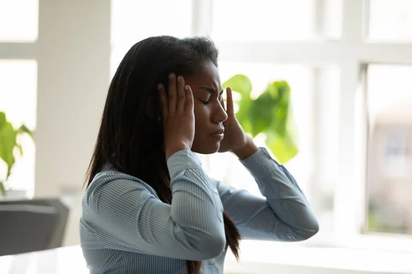 Mujer de negocios afroamericana infeliz que sufre de dolor de cabeza en el trabajo . —  Fotos de Stock