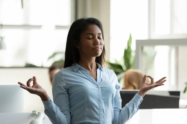 Satisfied african american businesswoman relaxing, meditating in yoga pose breathing exercises. — Stock Photo, Image