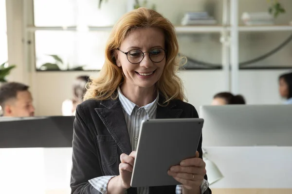 Feliz atractiva mujer de negocios madura usando tableta y recibiendo buenas noticias . — Foto de Stock