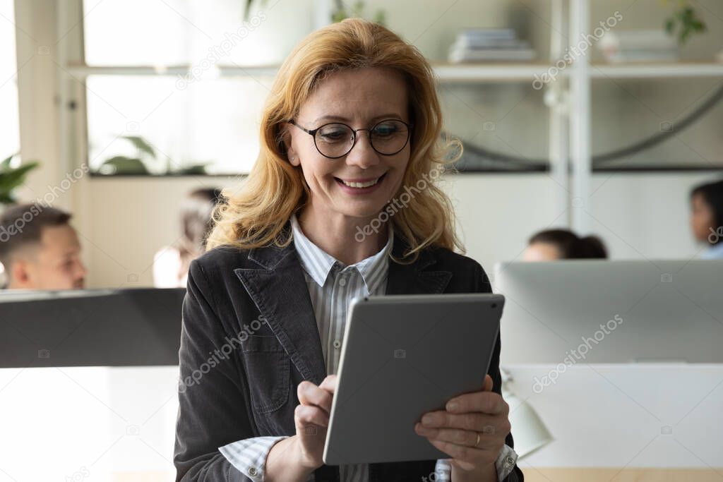 Happy attractive mature businesswoman using tablet and getting good news.