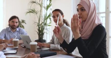 Gülümseyen genç Arap kadın çalışan iş arkadaşlarıyla iş konularını tartışıyor.