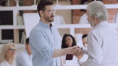 Kendinden emin orta yaşlı şirket sahibi, gülümseyen genç yöneticiyi övüyor..