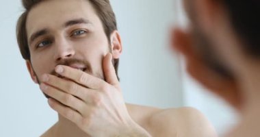 Genç yakışıklı adam aynaya bakarken sakala dokunuyor.