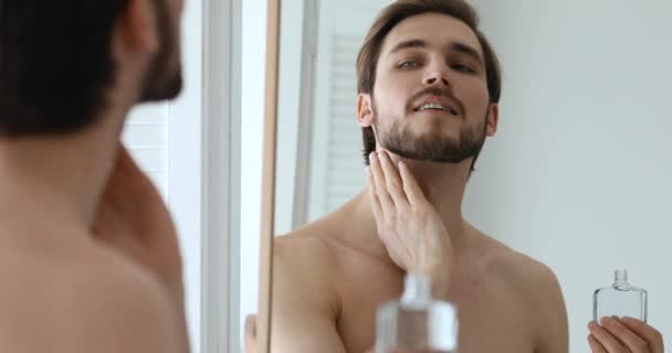 Sonriente joven guapo confiado aplicando loción de perfume aftershave — Vídeo de stock