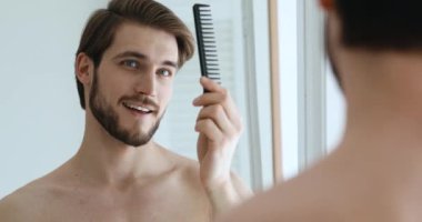 Kendine güveni tam genç bir adam tarak tutuyor saçlarını tarıyor ve aynaya bakıyor.