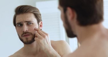 Aynaya bakan mutsuz bir adam cilt sorunundan endişeleniyor.