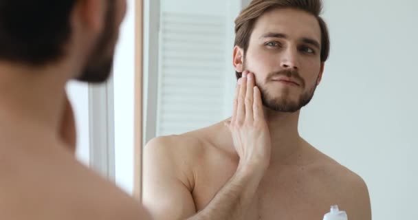 Zelfverzekerde man met baard die aftershave lotion op gezicht en hals aanbrengt — Stockvideo