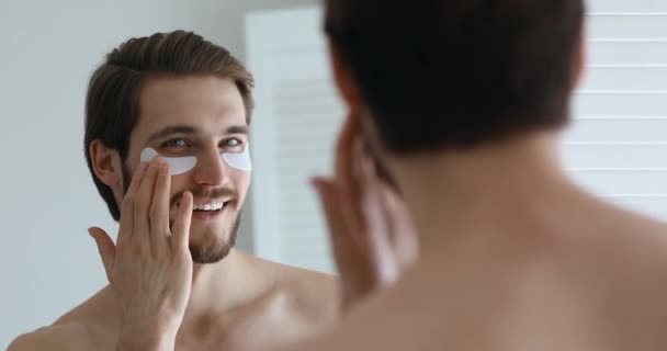 Gelukkig charmant jongeman toepassen undereye patches kijken in spiegel — Stockvideo