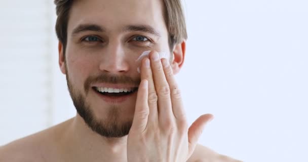 Happy charming metrosexual guy applying facial cream looking at camera — Stock Video