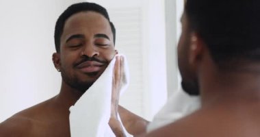 Mutlu Afrikalı adam aynaya bakarak yüzünü havluyla siliyor.