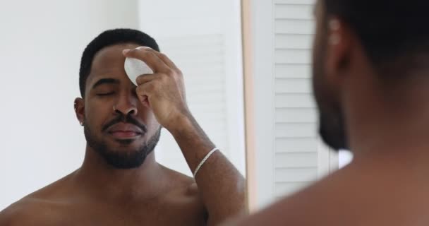 Bonito homem africano limpeza purificante pele facial segurando esponja esfoliante — Vídeo de Stock