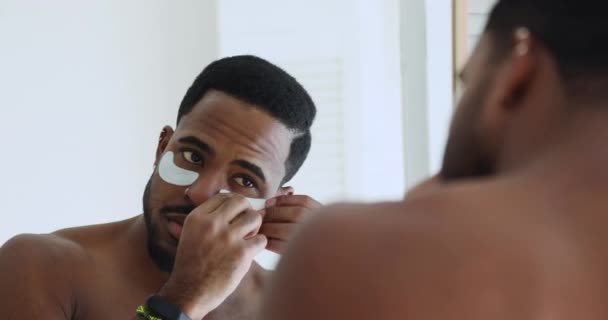 Metrosexual african man applying undereye patches looking in bathroom mirror — Stock Video