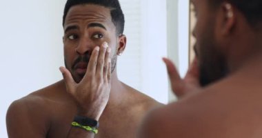 Genç Afrikalı adam aynaya bakarken yüzüne krem sürüyor.