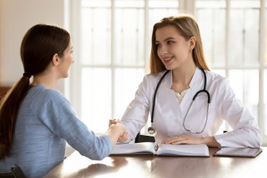 Muayenehanedeki gülümseyen doktor el sıkışan hasta.