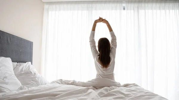 Pandangan belakang wanita duduk di tempat tidur mengangkat tangan peregangan tubuh — Stok Foto