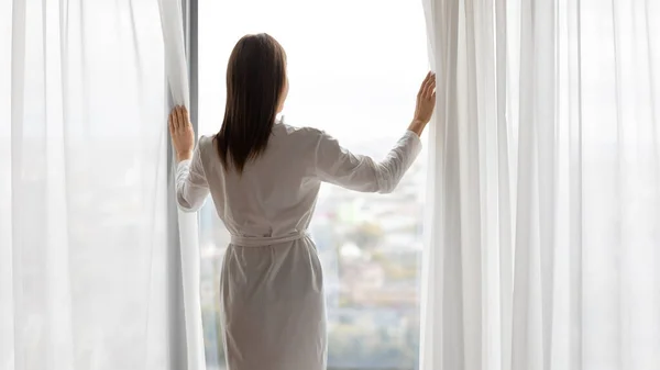 Wanita yang berdiri di dekat jendela menikmati pemandangan kota — Stok Foto