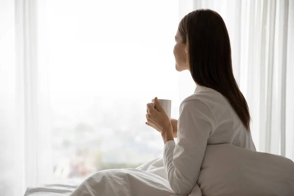 Wanita bangun duduk di tempat tidur memegang cangkir dengan teh — Stok Foto