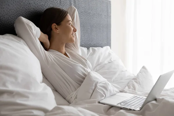 Woman lying in bed distracted from laptop usage looks away